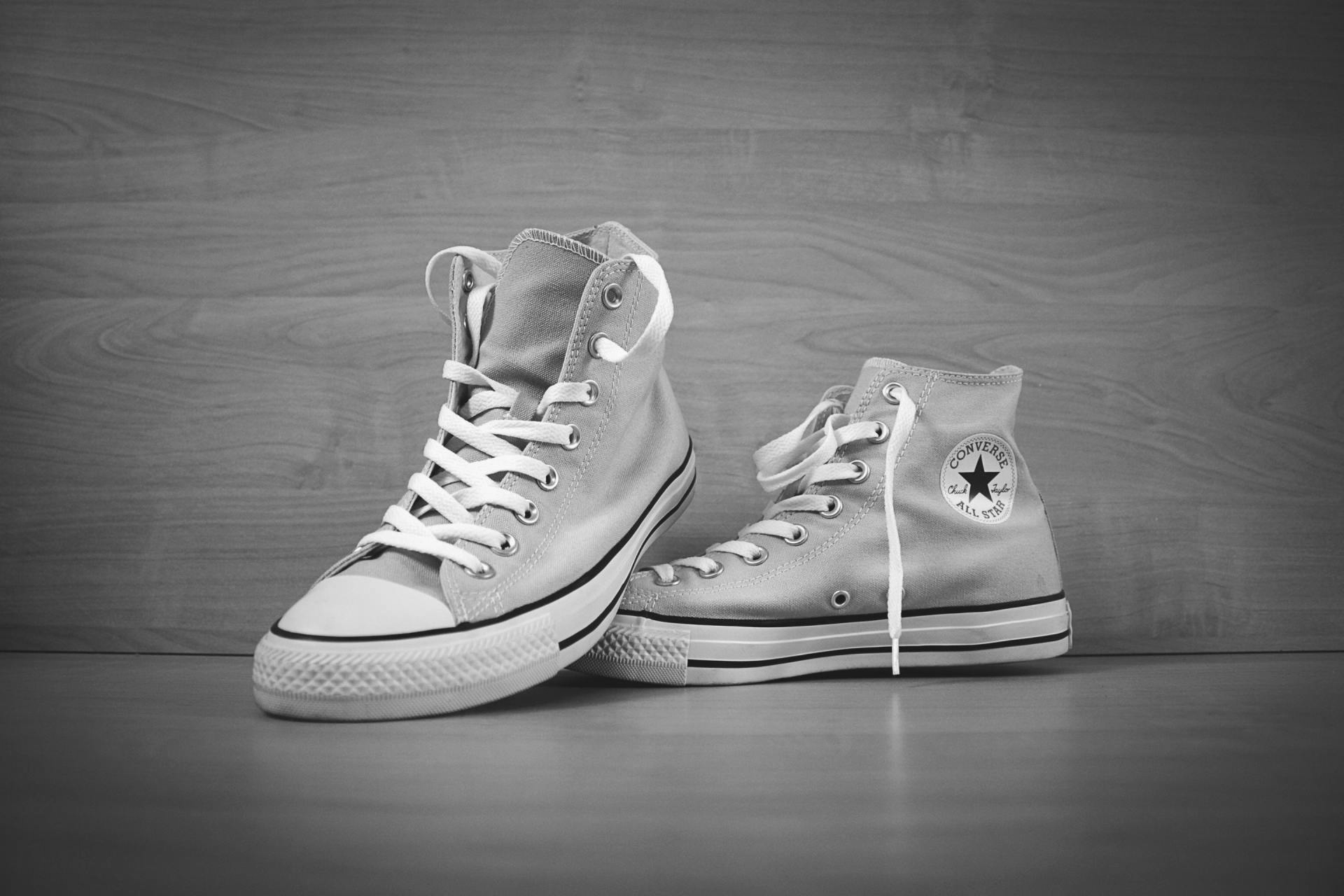 Two Converse sneakers on a wooden floor, one upright and one resting on its side.